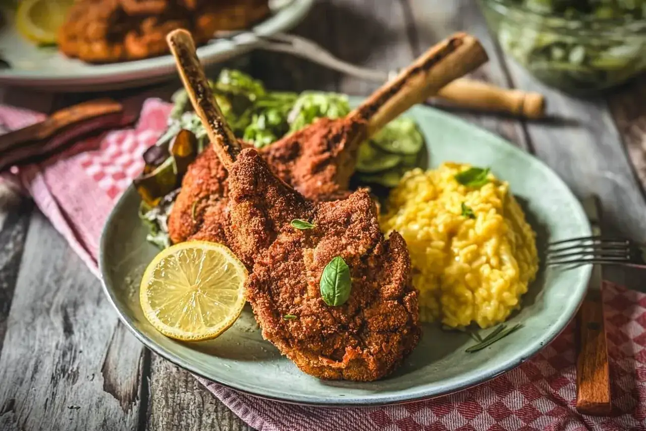 Zwei knusprige Kalbsschnitzel im italienischen Stil, serviert mit cremigem Risotto, Gurkensalat und Zitrone.