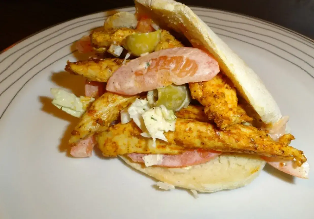 Pyszny kebab w picie z soczystym kurczakiem, świeżymi warzywami i kremowym sosem, podany na białym talerzu.