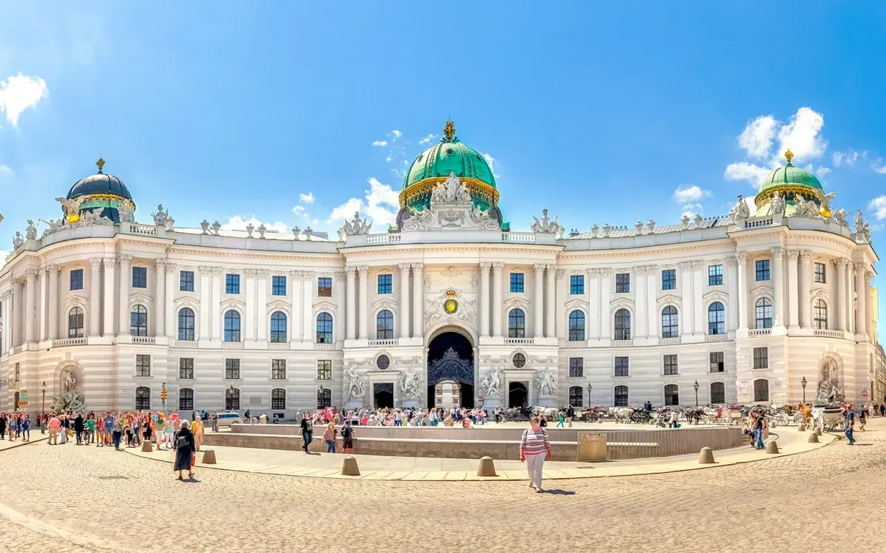 Majestatyczny pałac Sisi w Wiedniu, z zieloną kopułą i tłumem turyst&oacute;w na placu.