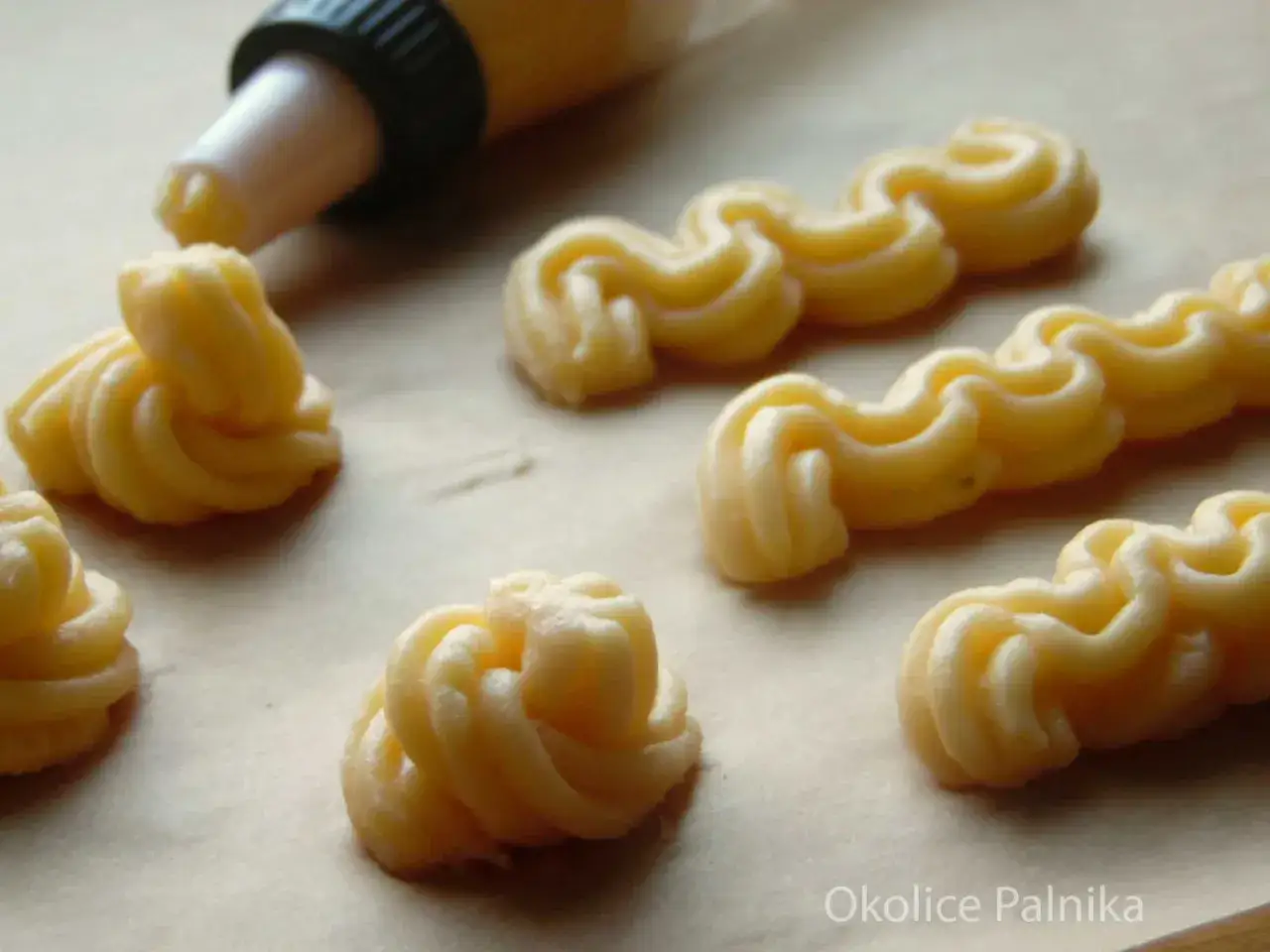 Kremowe eklery z czekoladą i profiteroles w trakcie formowania. Widać rękaw cukierniczy i uformowane ciasto.