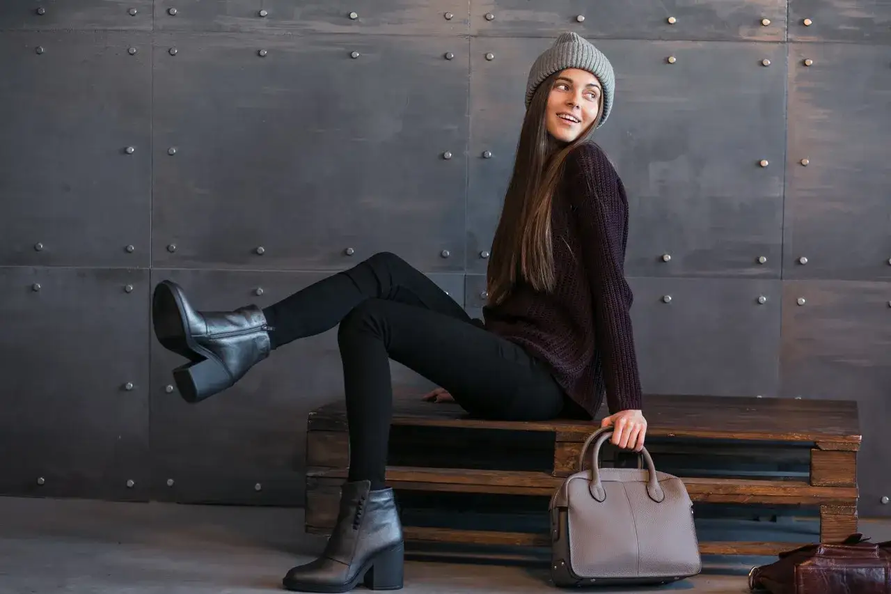 Dziewczyna w czarnych rurkach i swetrze, z szarym beanie, pokazuje, jakie spodnie do sztybletow pasują idealnie.