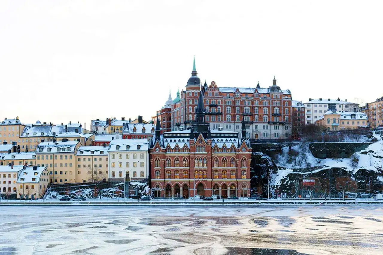 Vinter i Stockholm. Sn&ouml;kl&auml;dda byggnader l&auml;ngs en isig strandkant.