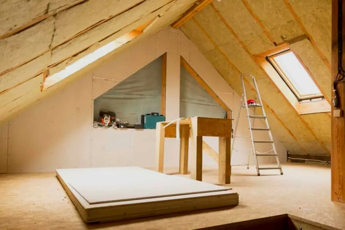 A &aacute;tico en construcci&oacute;n, con aislamiento en el techo y paredes de yeso. Hay una escalera, una mesa de trabajo y materiales de construcci&oacute;n. Se siente el fr&iacute;o en casa.