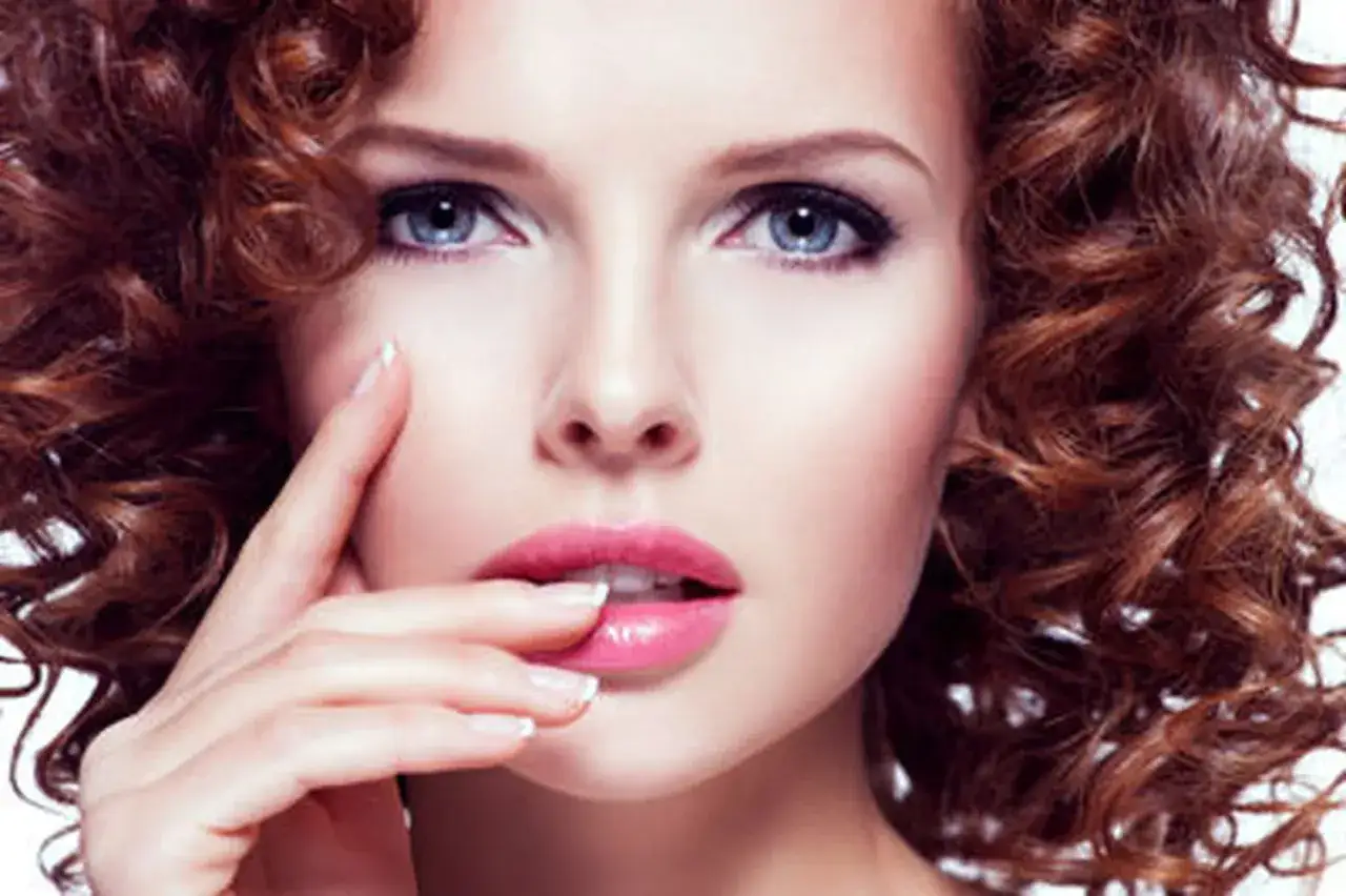 Une femme &agrave; la peau claire et aux yeux bleus arbore une chevelure rousse boucl&eacute;e. La couleur de cheveux parfaite pour sa peau claire et ses yeux bleus.