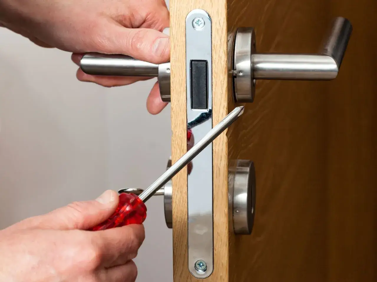 Main tenant installe une serrure sur une porte de chambre. Un tournevis est utilisé pour fixer la poignée.