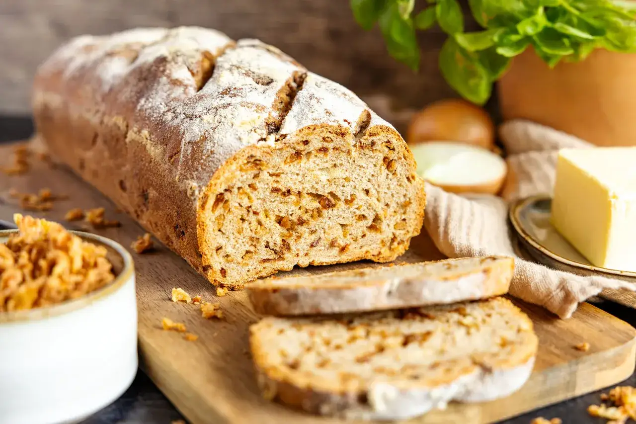 Ein frisch gebackenes Zwiebelbrot mit knusprigen Röstzwiebeln, bereit für ein köstliches Zwiebelbrot Rezept. Daneben Butter und Zwiebeln.