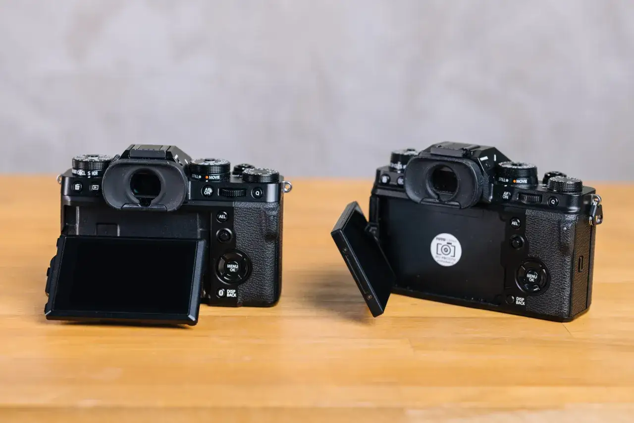 Dwa aparaty Fujifilm X-T5 na drewnianym stole. Jeden z nich ma uchylony ekran, drugi jest zamknięty.