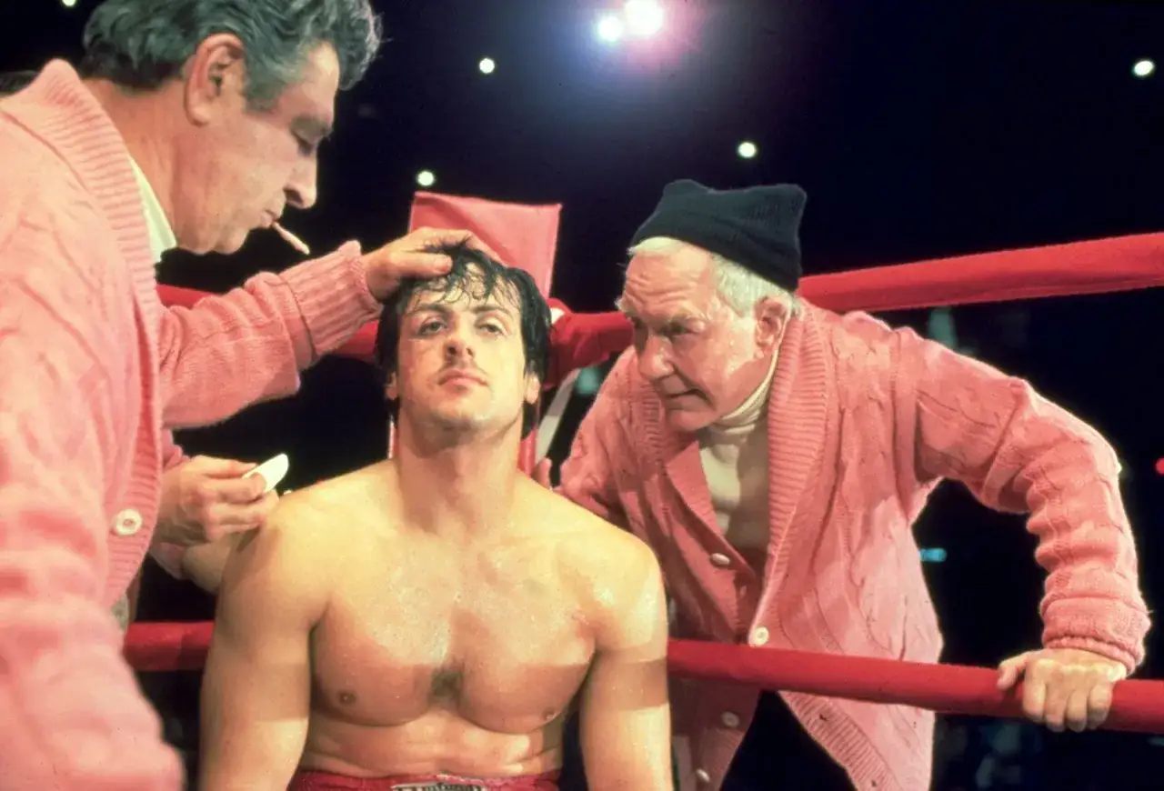 Rocky Balboa, med smuts och s&aring;r i ansiktet, f&aring;r omsorg av Mickey och Paulie i ringh&ouml;rnan. Rollistan i Rocky &auml;r ikonisk.