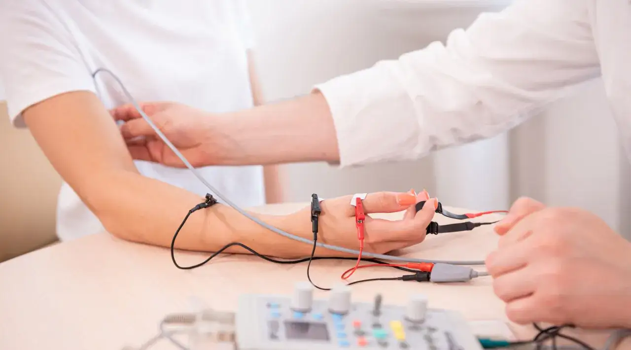Badanie EMG, co to jest? Elektromiografia ocenia funkcję nerwów i mięśni. Na ręce pacjentki widoczne są elektrody podłączone do aparatury.