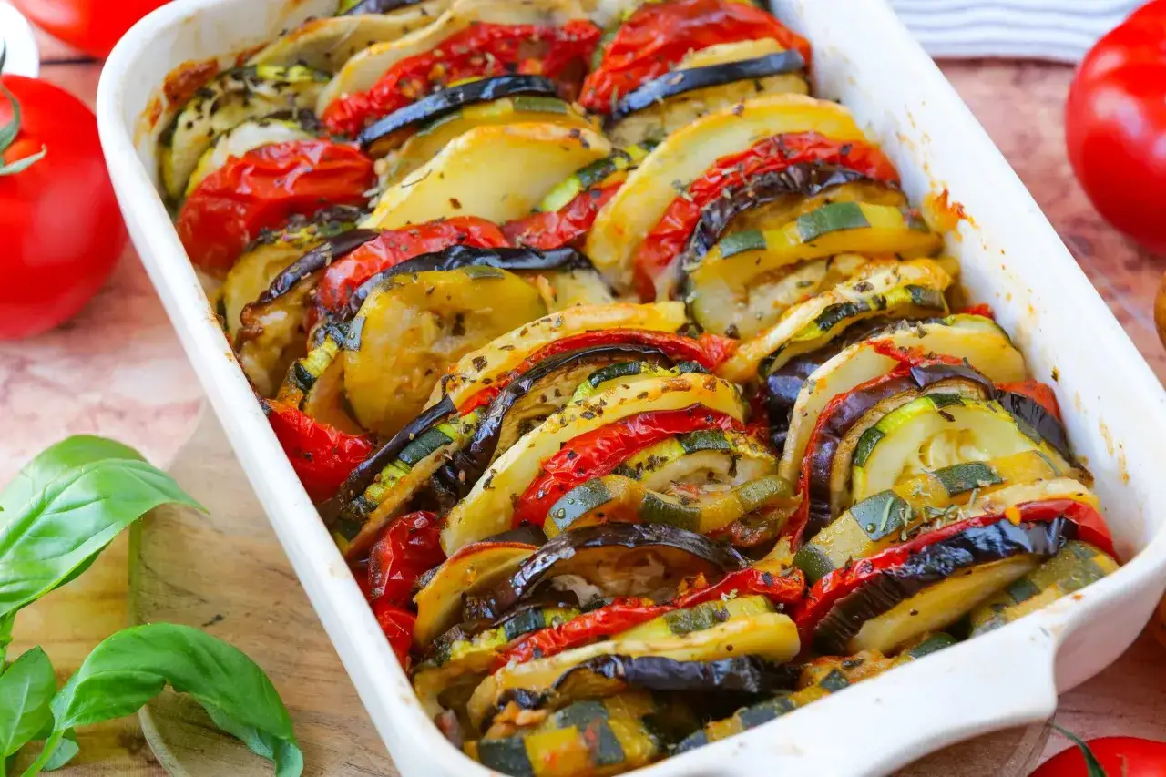 Un plat de tian de légumes coloré, avec des rondelles de courgettes, aubergines et tomates disposées en éventail, prêt à être dégusté.