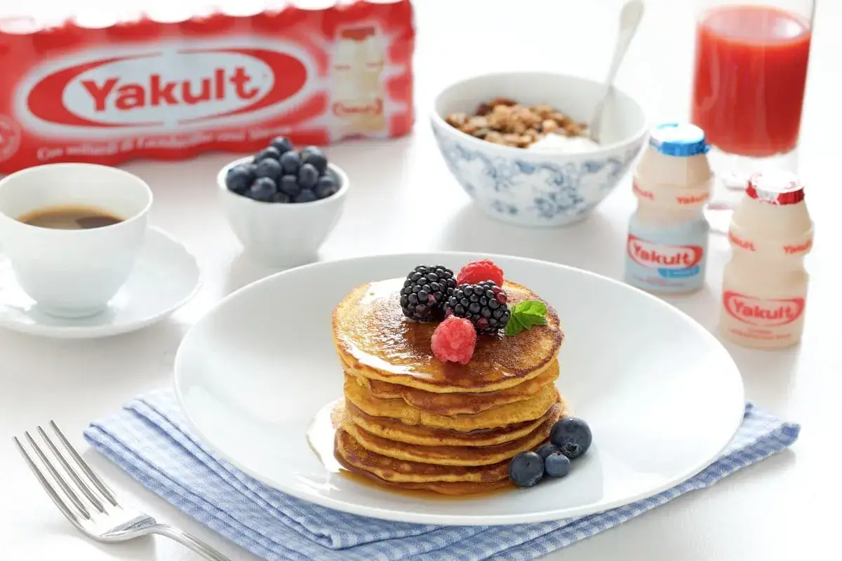 Pancakes con farina di avena, guarniti con frutti di bosco, serviti con caff&egrave;, mirtilli, yogurt e Yakult.