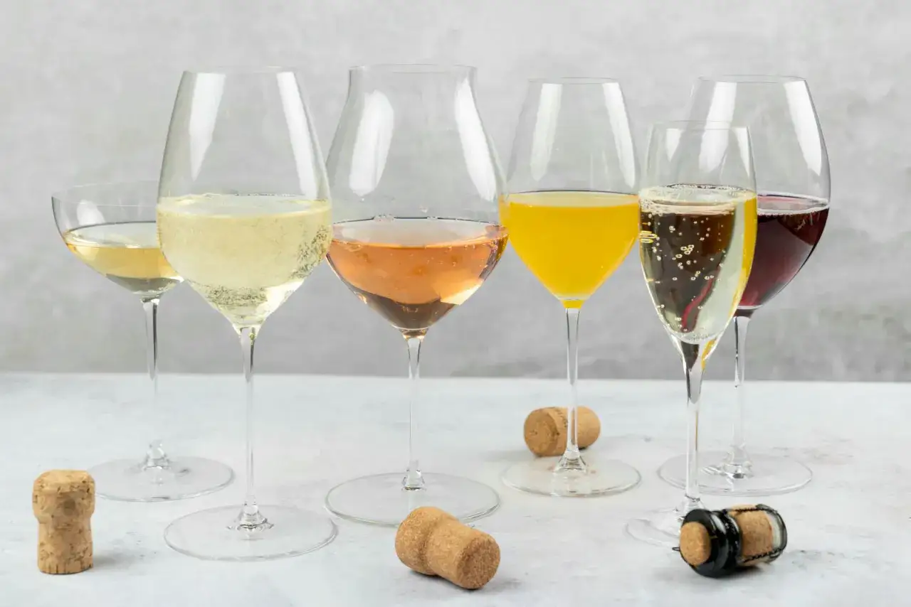 Fem glas med bubbel, fr&aring;n ljusgult till m&ouml;rkr&ouml;tt, och korkar p&aring; bordet. En festlig samling av pet nat.