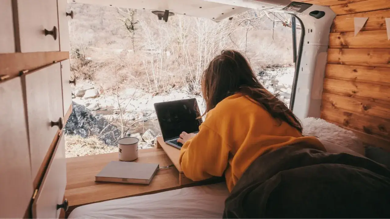 Kto to nomadzi? Kobieta pracuje na laptopie w kamperze, otoczona naturą. Wolność i praca w drodze.
