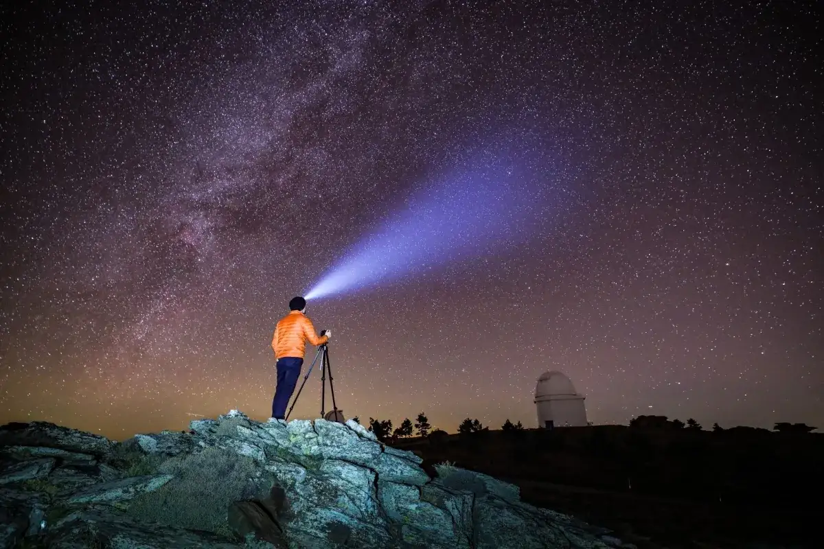 Astronom fotografuje nocne niebo z Canon EOS Ra. Latarka na głowie oświetla drogę.