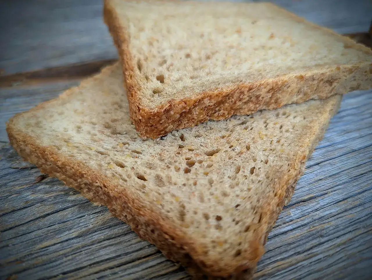 Zwei Scheiben Vollkorntoastbrot liegen auf einer Holzoberfl&auml;che. Perfekt f&uuml;r ein einfaches toastbrot rezept.