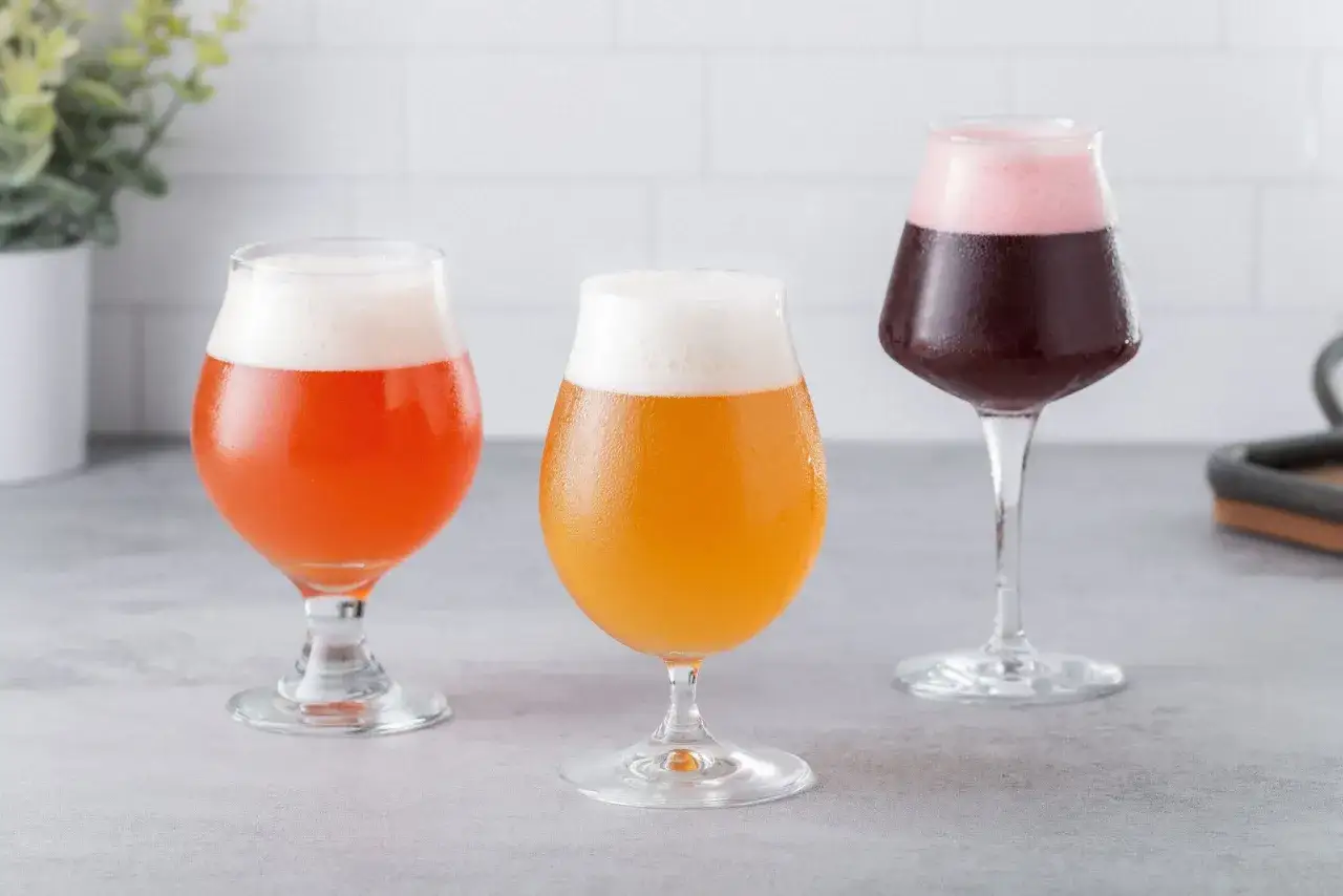 Trois verres de bi&egrave;re acide aux couleurs vives : rouge orang&eacute;, jaune dor&eacute; et pourpre avec une mousse rose.