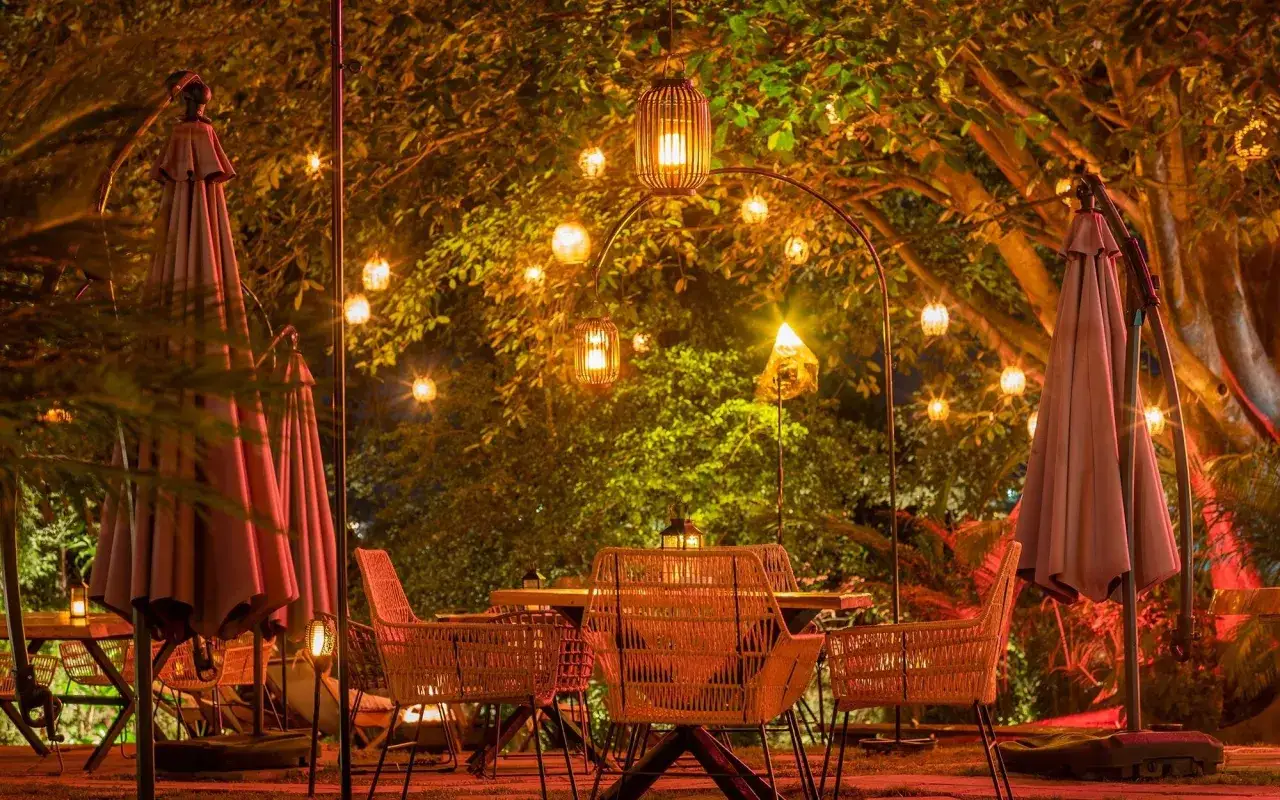 Gemütliche Gartenparty-Ideen: Tische & Stühle aus Rattan unter Lichterketten und Bäumen.