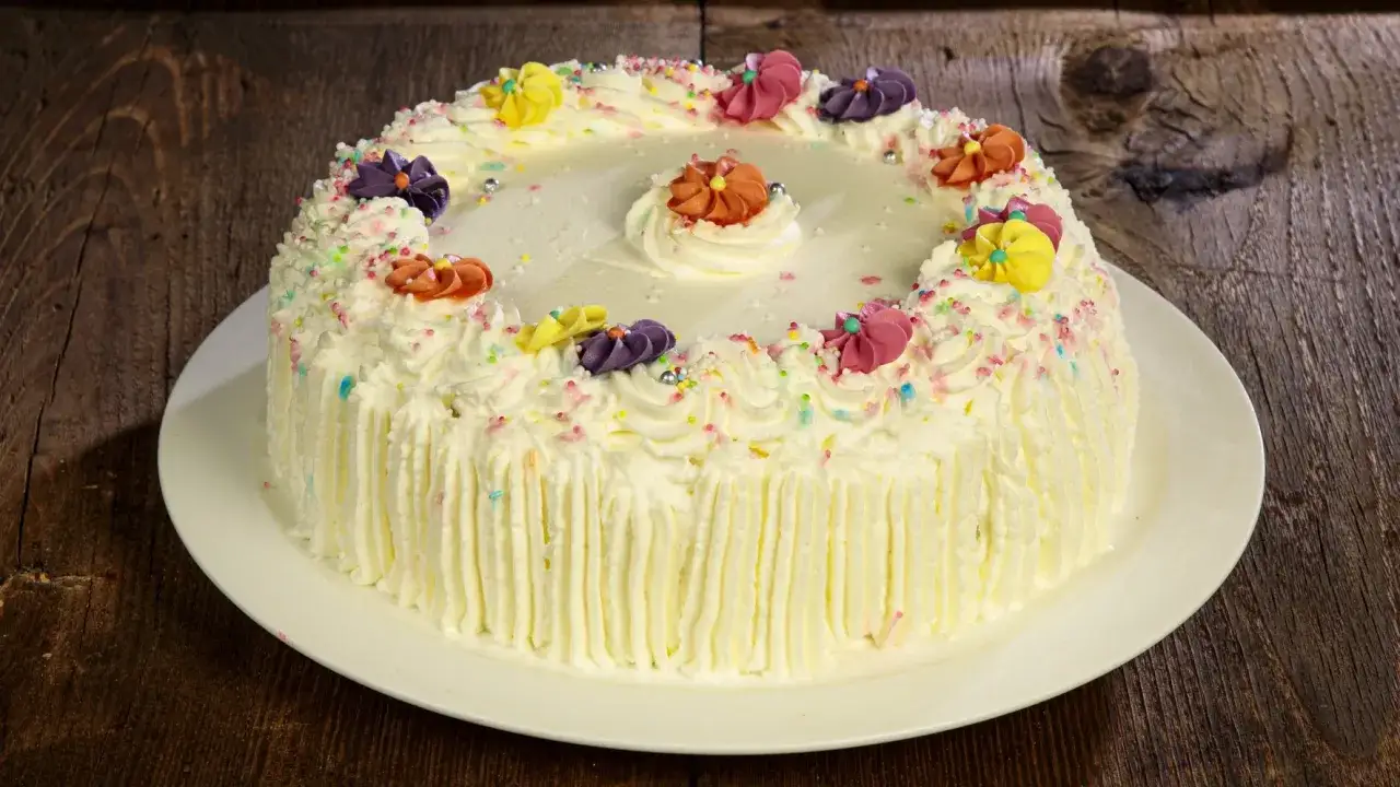 Torta decorata con panna, confettini colorati e fiori di glassa, una delle torte più buone da fare in casa.