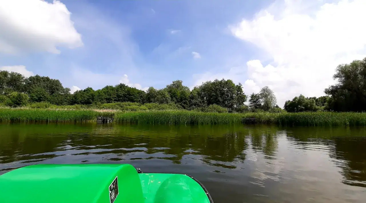 Zielona ł&oacute;dka na spokojnym jeziorze Bardze. W tle bujna roślinność i błękitne niebo z chmurami.