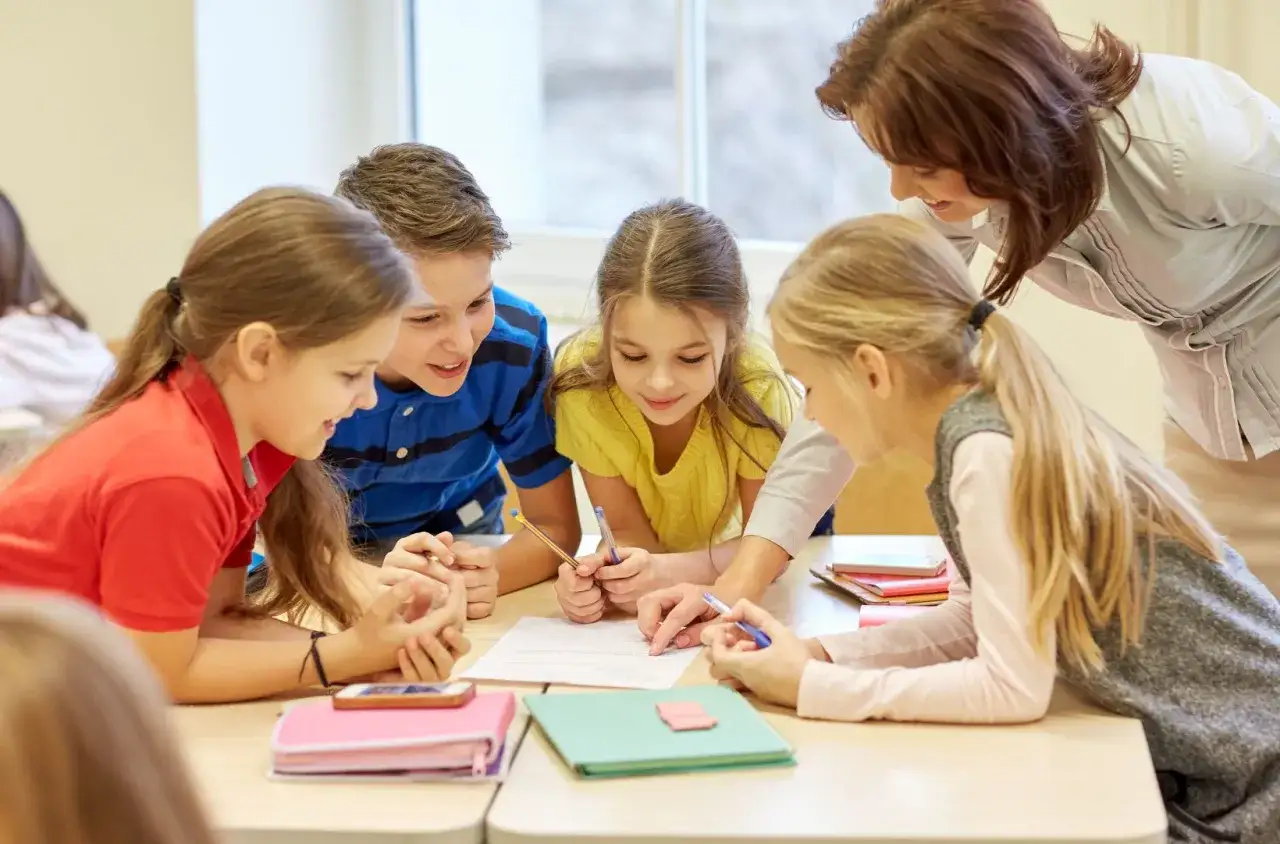 Nauczycielka pomaga uczniom z dysleksją objawy, pracując nad zadaniem. Dzieci skupione na kartkach.