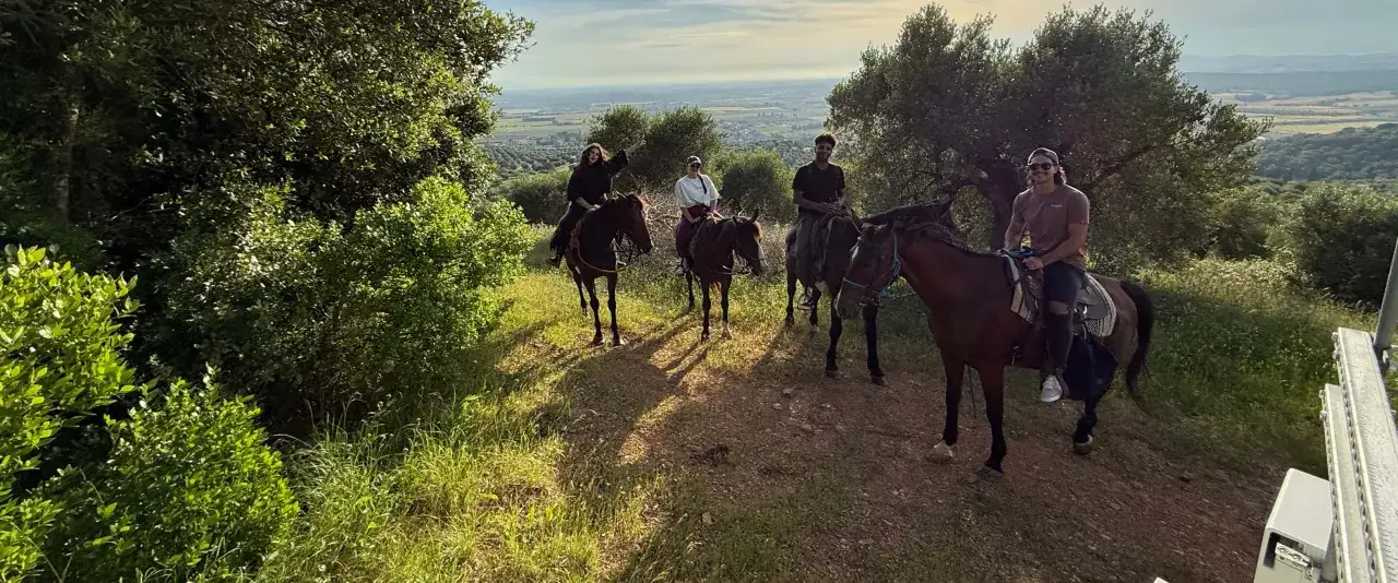 Un gruppo di persone vive una splendida passeggiata a cavallo toscana, godendosi il panorama collinare al tramonto.