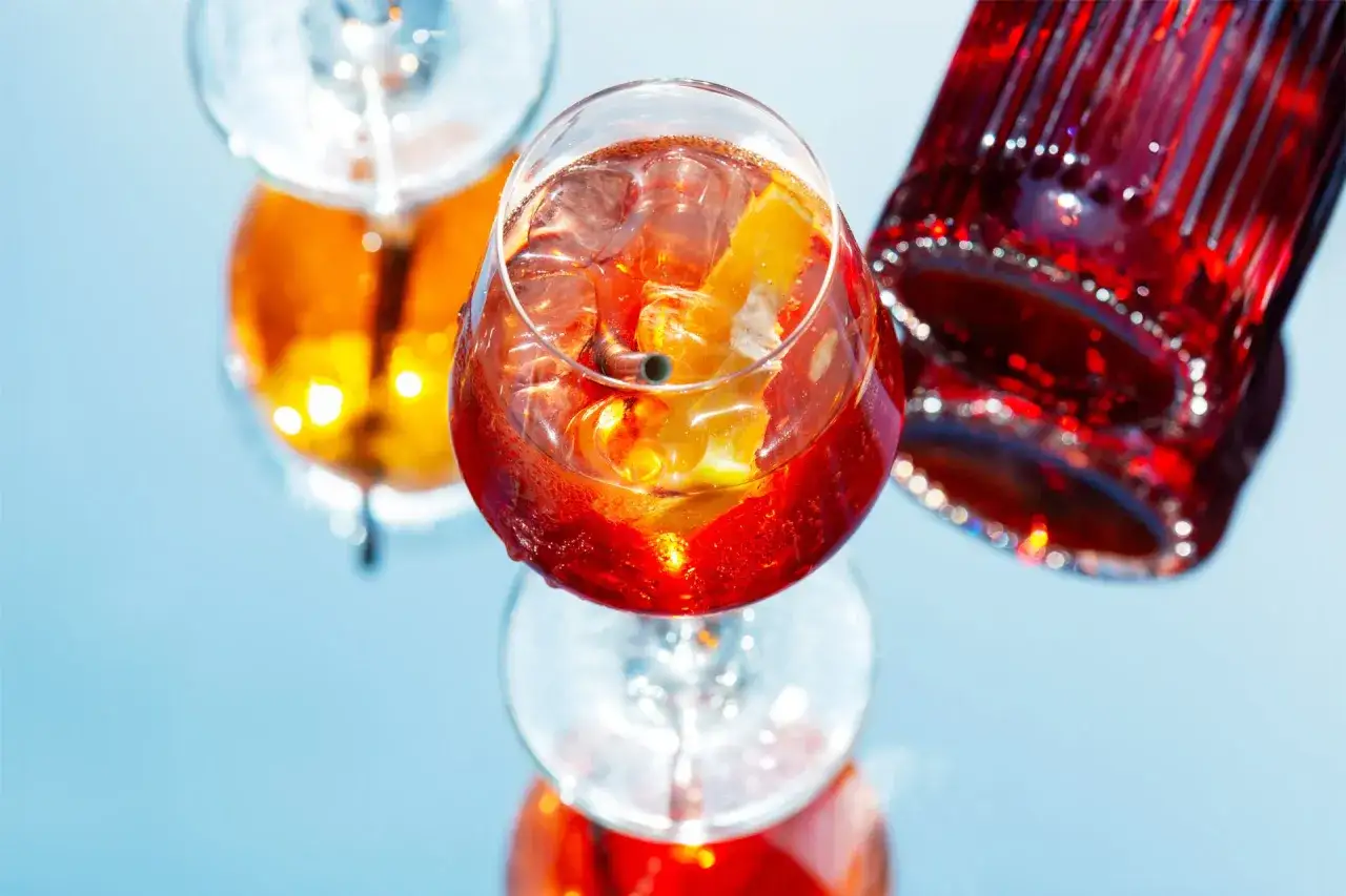 En Campari Spritz med is och apelsinskiva, bredvid en Campari-flaska.