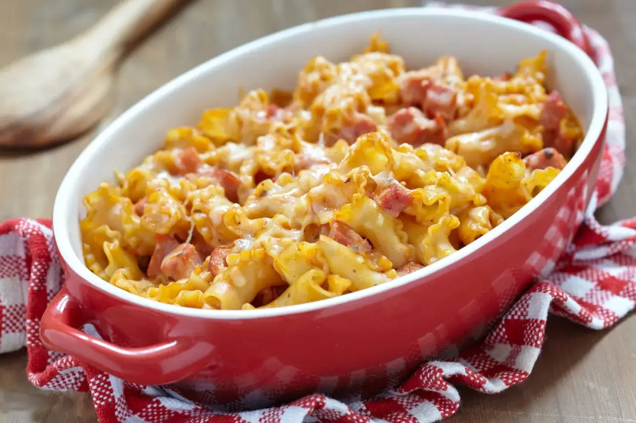 Un plat de pâtes coquillettes au jambon, gratiné au fromage, servi dans un plat rouge. Un délice réconfortant.
