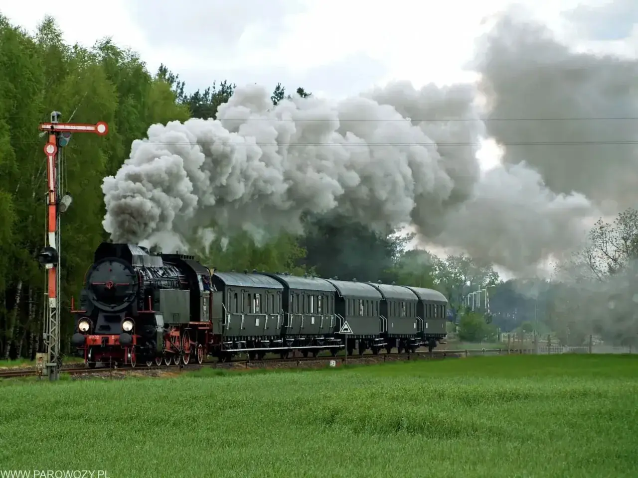 Parowóz z wagonami, kłęby dymu, semafor kolejowy. Pociąg retro rusza zgodnie z rozkładem jazdy.