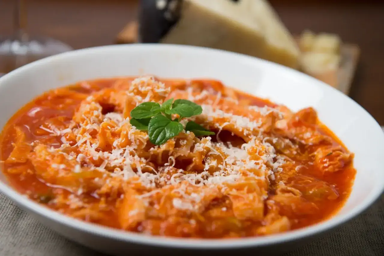 Trippa alla romana, uno dei piatti tipici del Lazio, servita in una ciotola bianca con parmigiano grattugiato e una fogliolina di menta.