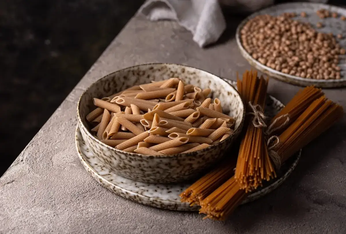 Makaron pełnoziarnisty penne w misce obok spaghetti z ciecierzycy. Dwa rodzaje makaronu grahan vs duru.