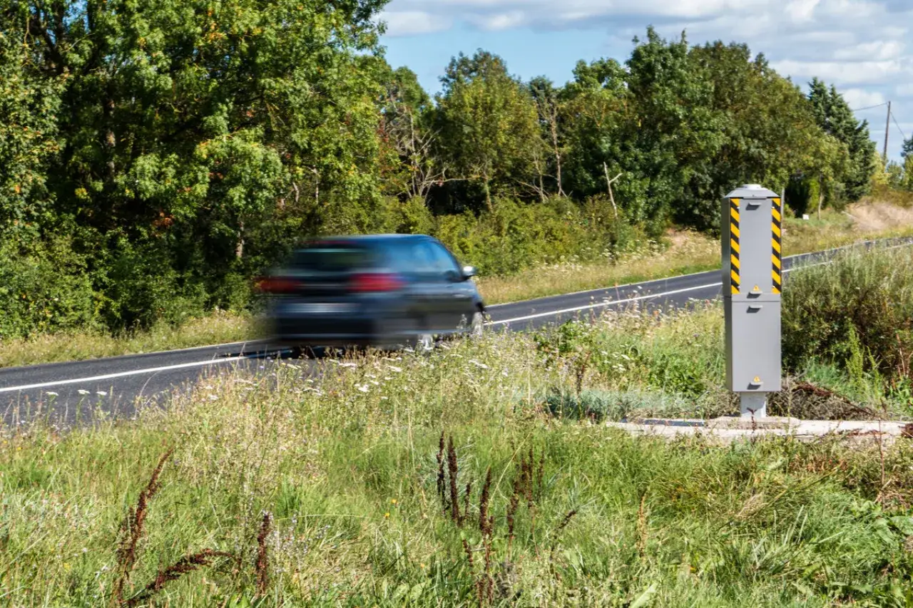 Un radar tagué peut-il flasher ? Une voiture passe à toute vitesse devant un radar de vitesse, entouré de verdure luxuriante.