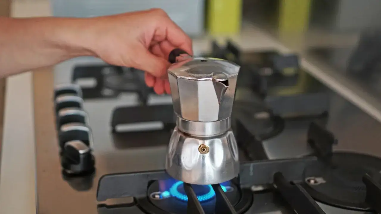 Una mano posiziona una moka sul fornello acceso, mostrando come funziona la moka per un caffè aromatico.