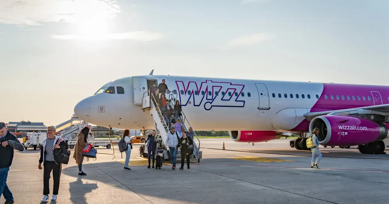 Pasażerowie schodzą po schodkach z samolotu Wizz Air. Wizz priority to szybka droga do celu.