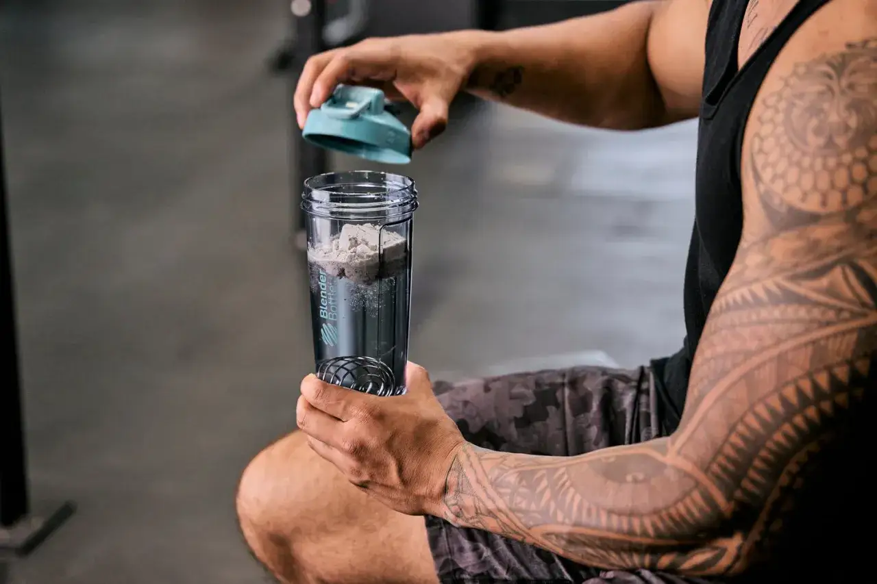 Mann mit t&auml;towiertem Arm bereitet Proteinshake vor. Die Frage 