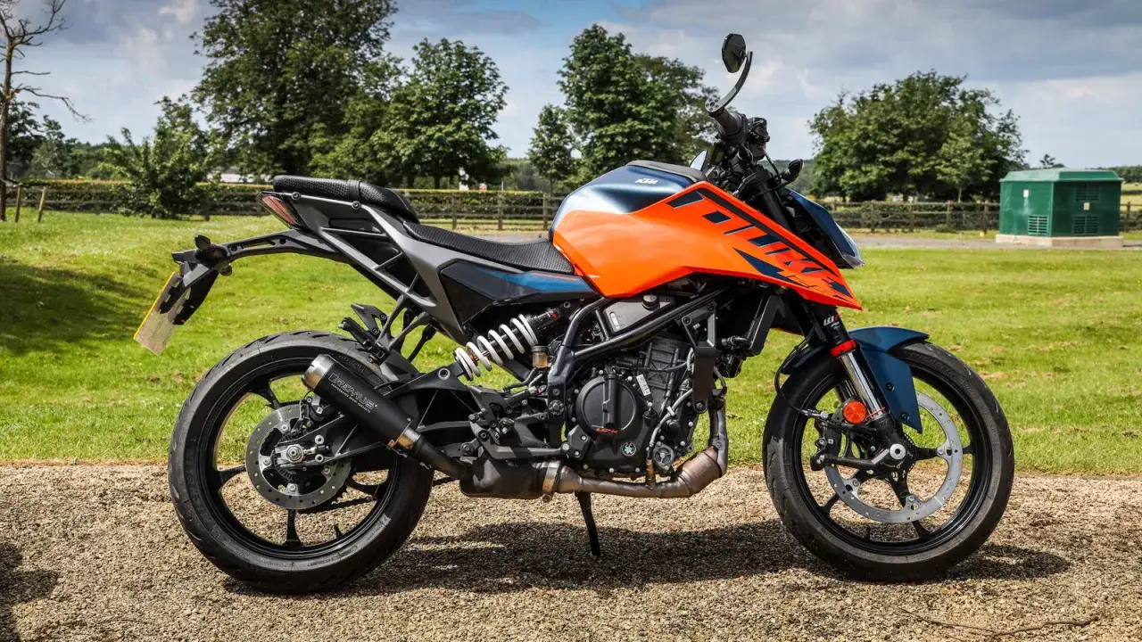 Pomarańczowo-niebieski KTM, najmocniejszy motocykl na kat B, stoi na żwirowej drodze. W tle zielona łąka i drzewa.