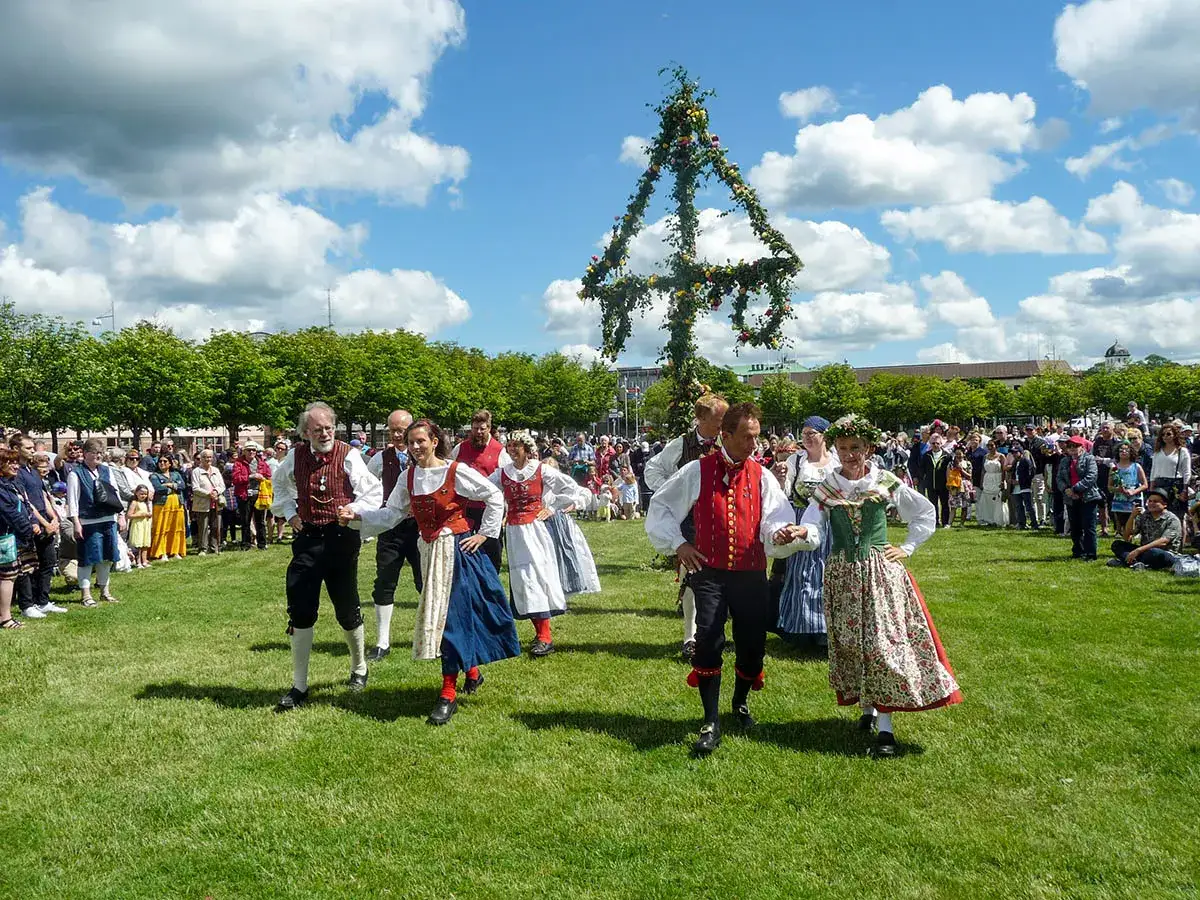Midsommarfirande i Sverige med folkdansare runt en blomsterprydd midsommarstång.