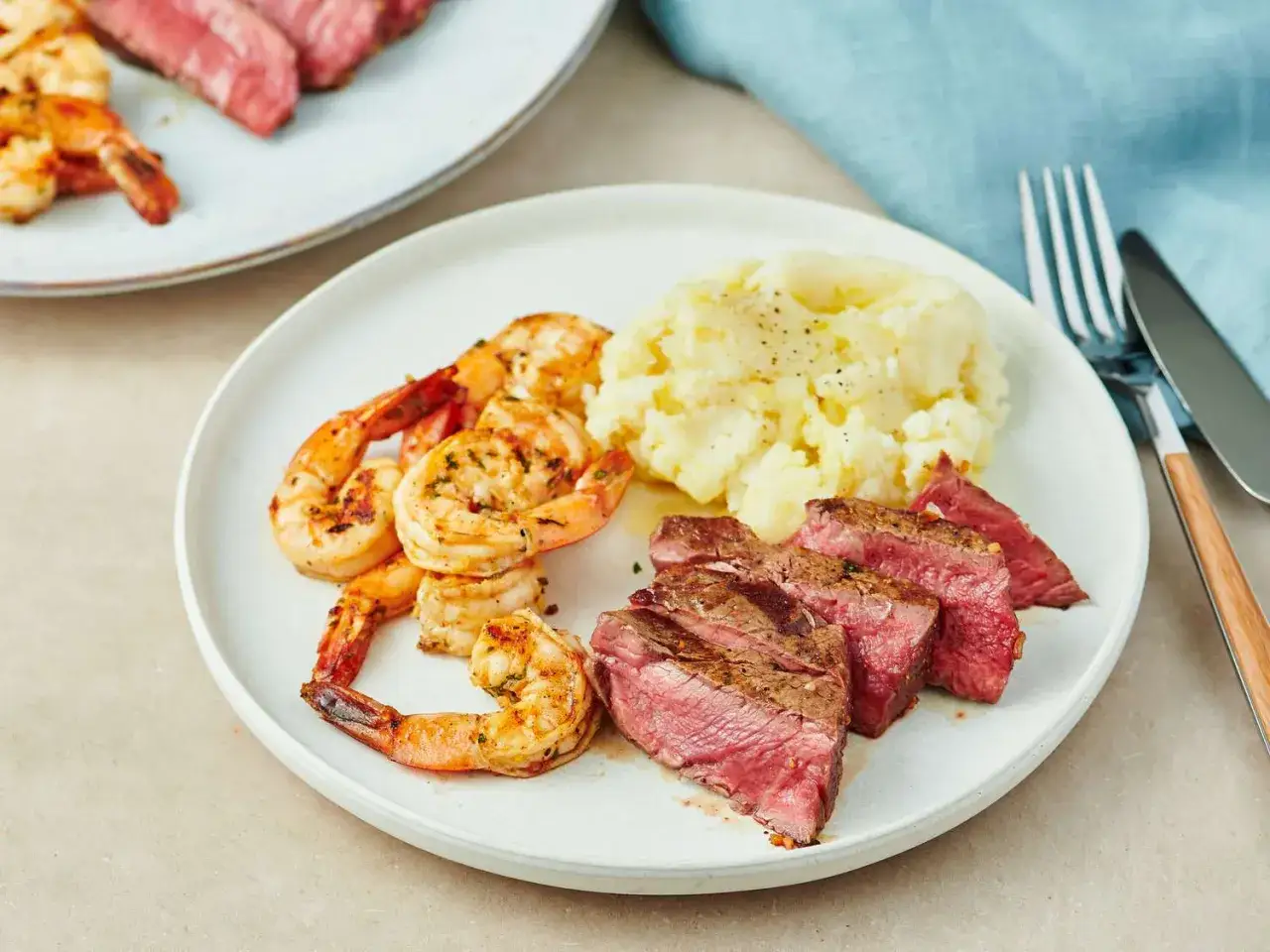 En tallrik med saftigt surf and turf: grillade r&auml;kor, skivad biff och kr&auml;migt potatismos.