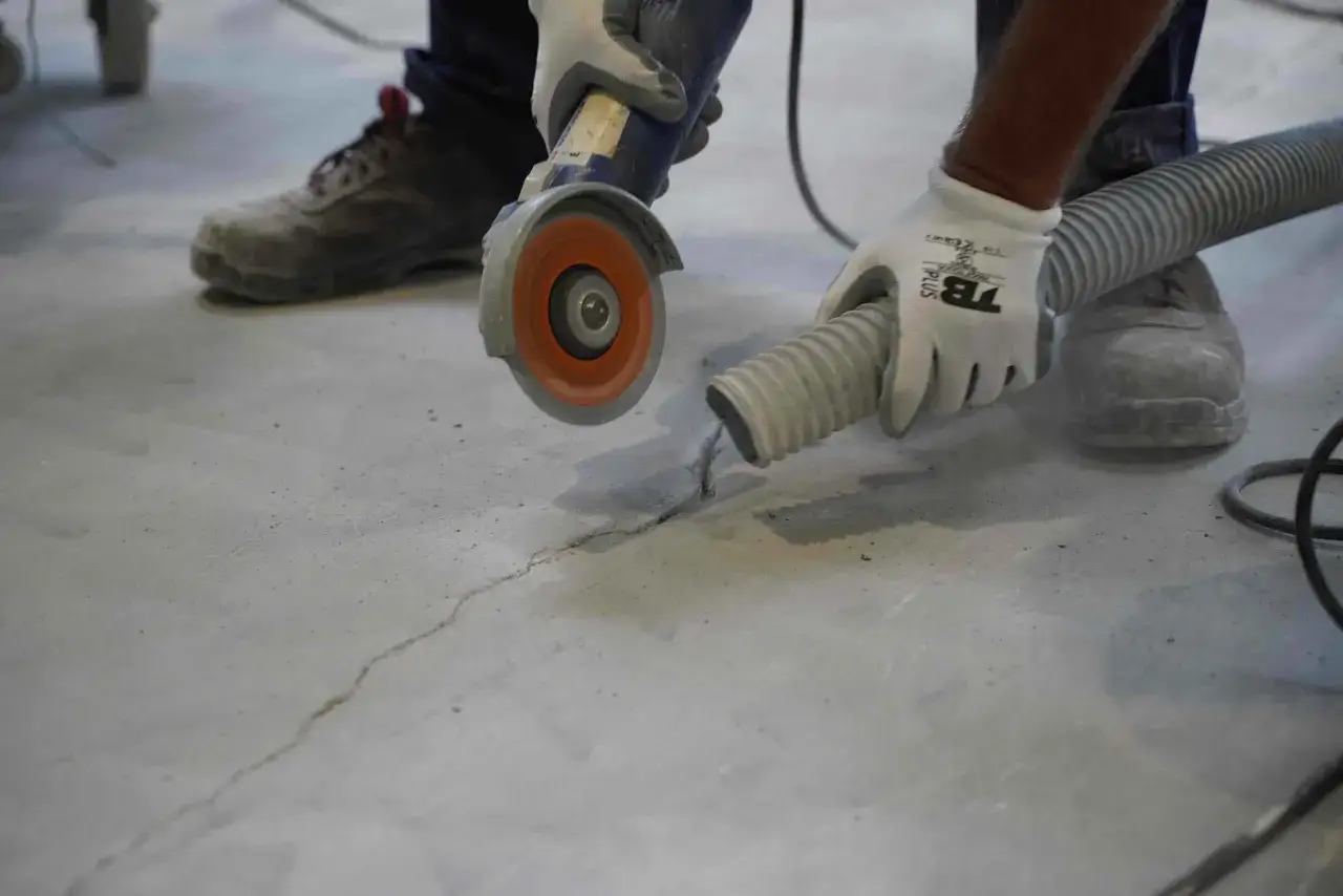 Trabajador realiza reparaci&oacute;n de fisuras en soleras de hormig&oacute;n con amoladora y aspiradora.