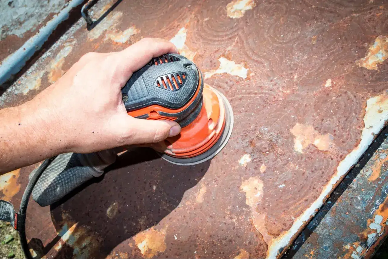 Hand schleift Rost von Metall, um es für das Lackieren vorzubereiten.