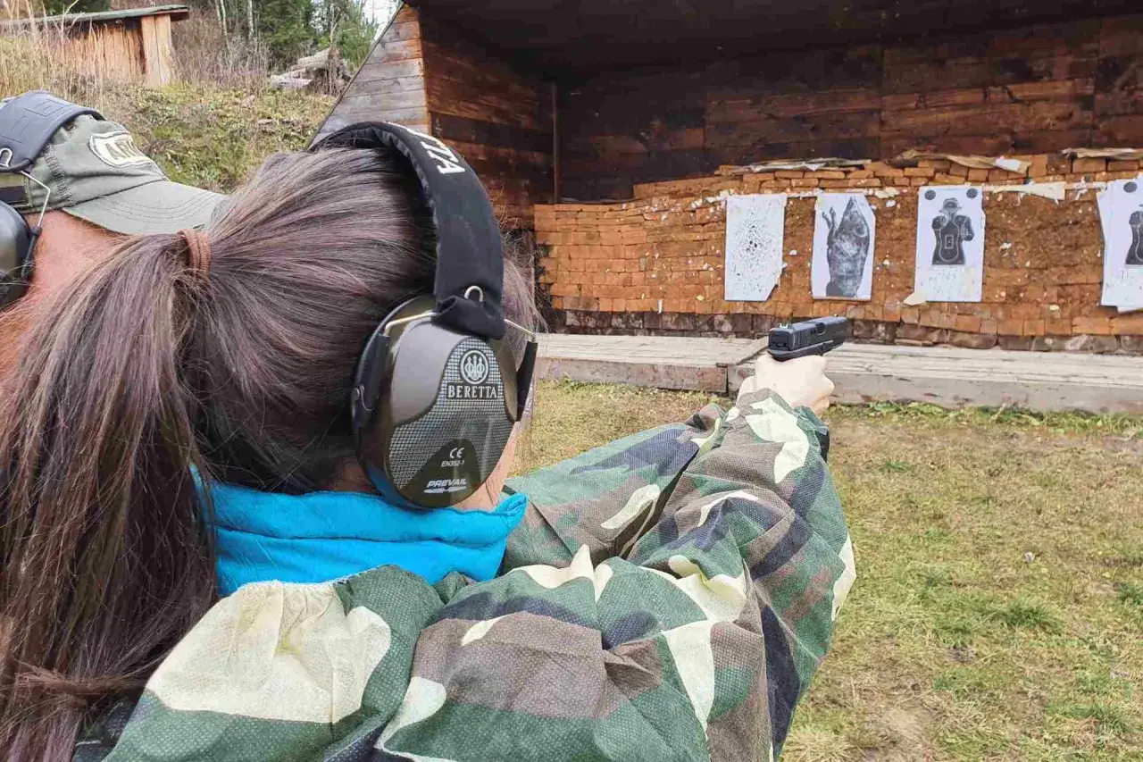 Dziewczyna w słuchawkach ochronnych ćwiczy strzelanie z broni na strzelnicy.