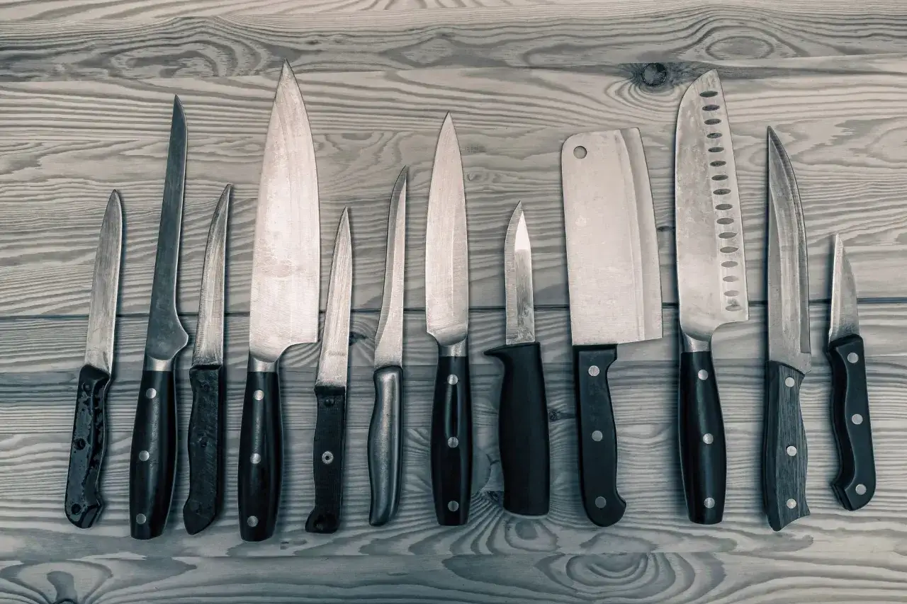 Una colecci&oacute;n de cuchillos de cocina, incluyendo un cuchillo daga, dispuestos sobre una tabla de madera.
