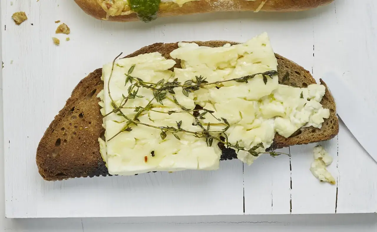Ein St&uuml;ck schwarzbrot toasten und mit cremigem K&auml;se und frischem Thymian belegen.