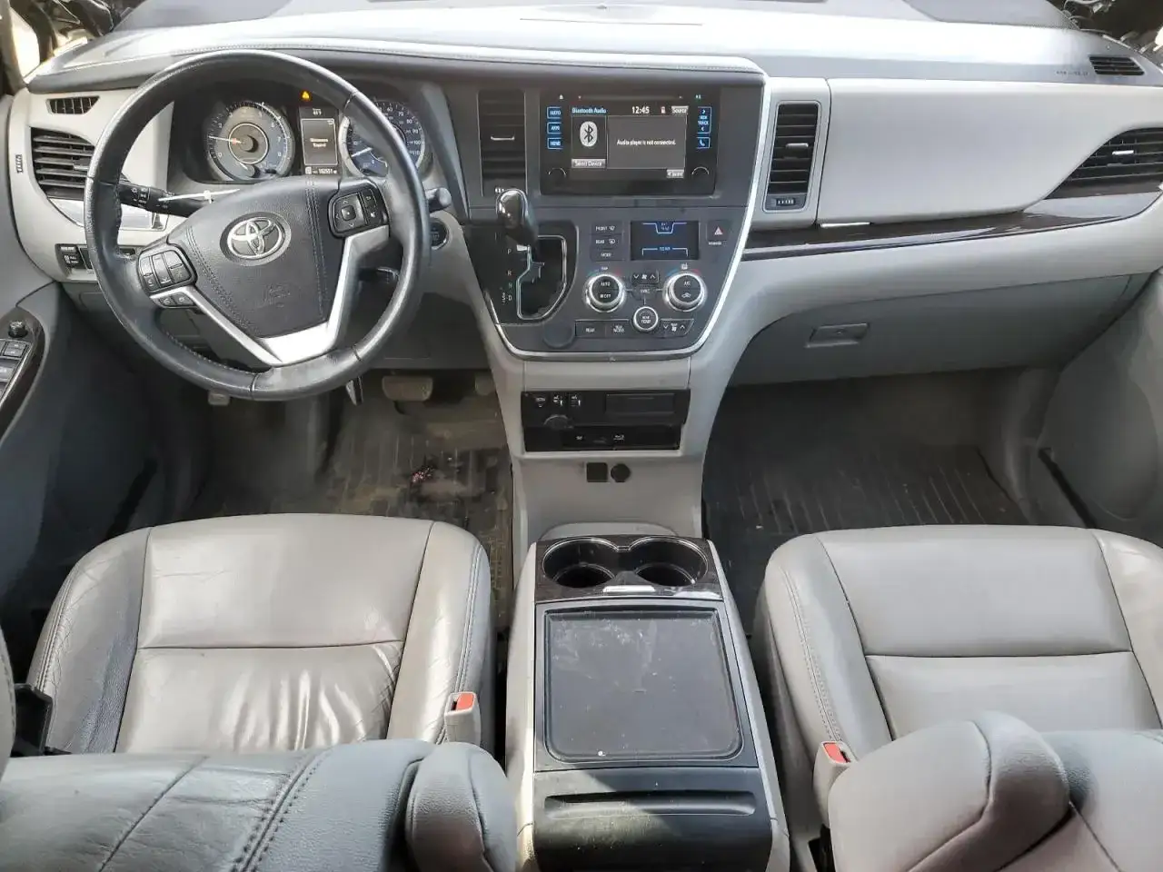Wnętrze Toyoty Sienna 2025: szare skórzane fotele, kierownica, deska rozdzielcza z ekranem multimedialnym i konsola środkowa.