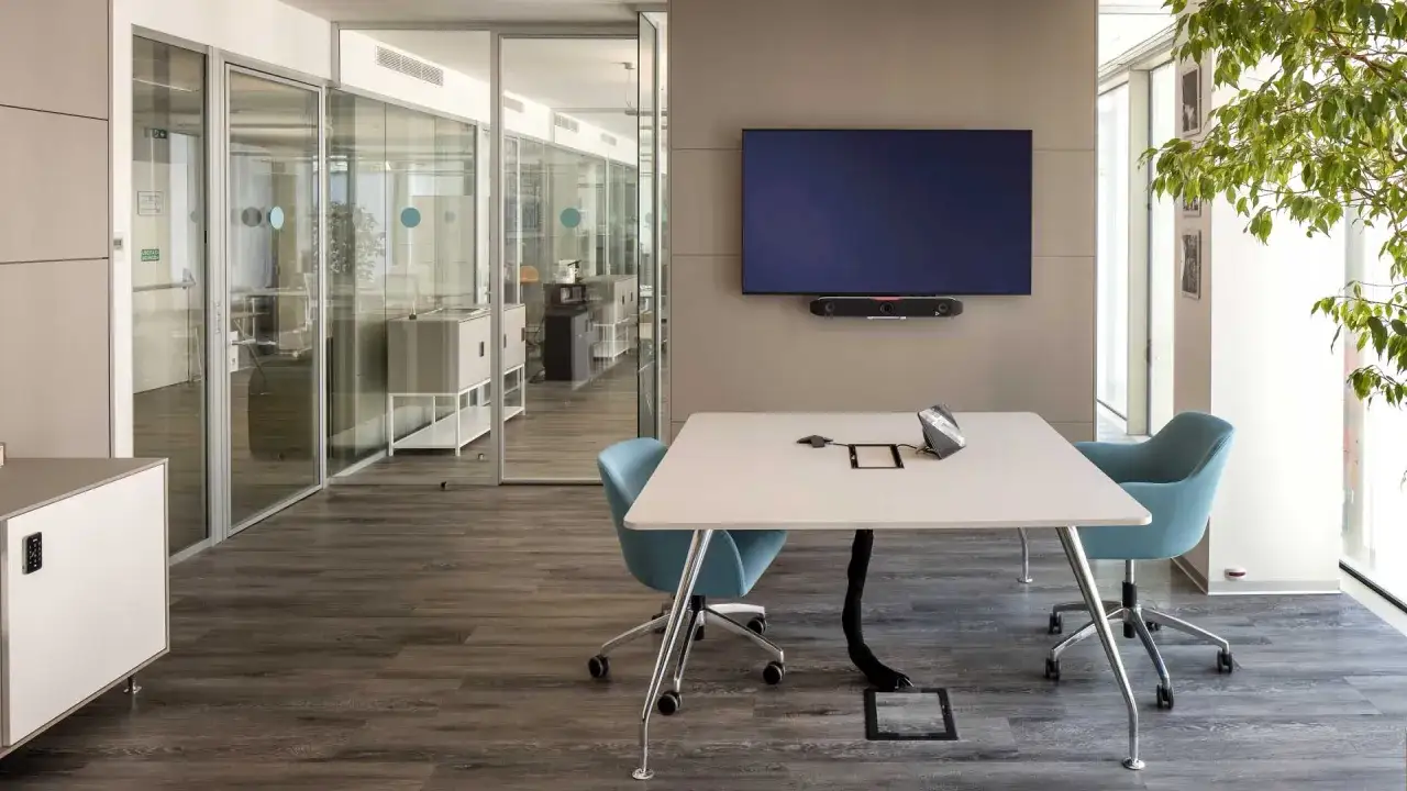 Bureau moderne avec table de conf&eacute;rence, &eacute;crans, fauteuils bleus et plantes vertes. Une ambiance qui refl&egrave;te la tendance d&eacute;co bureau professionnel.