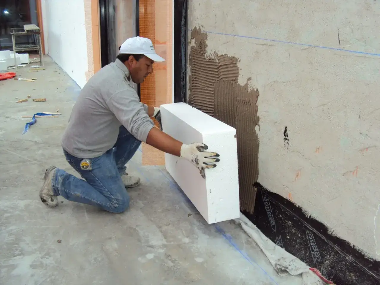 Obrero coloca pieza de aislante térmico exterior en pared.