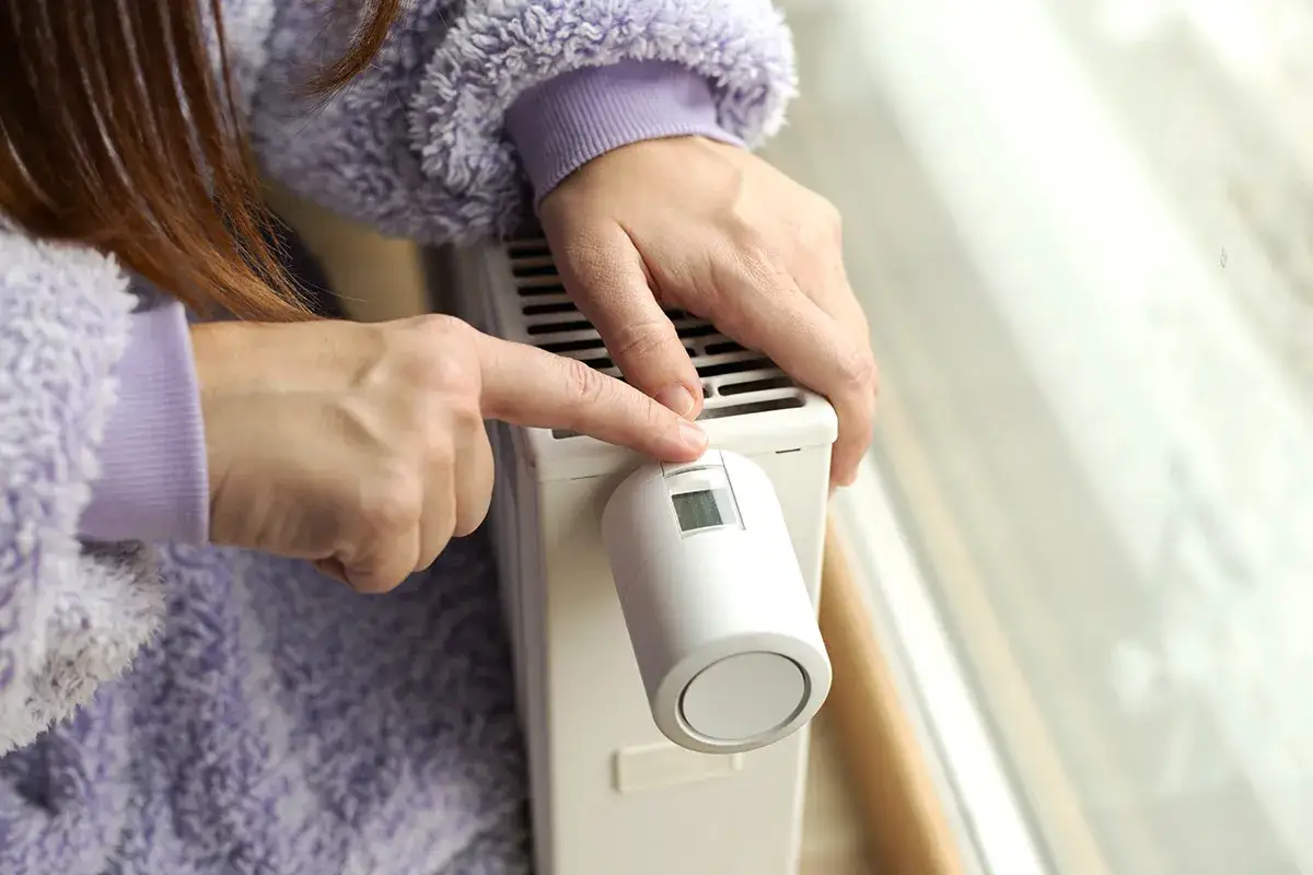 Mani che regolano la valvola di un termosifone, sperando che i termosifoni non si scaldino pi&ugrave;.