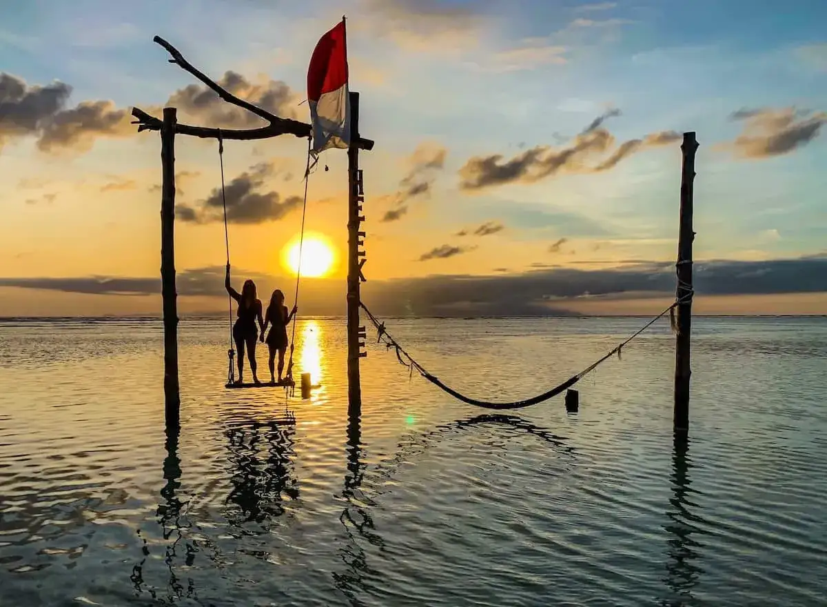 Två personer på en gunga vid solnedgången på Gili Air. Indonesiska flaggan vajar i bakgrunden.