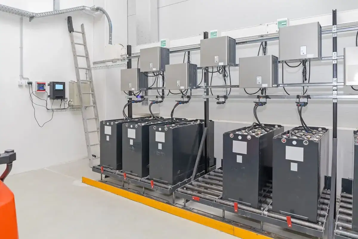 Instalaci&oacute;n de bater&iacute;as solares en un almac&eacute;n. Se ven grandes bater&iacute;as negras conectadas a unidades de control en la pared.