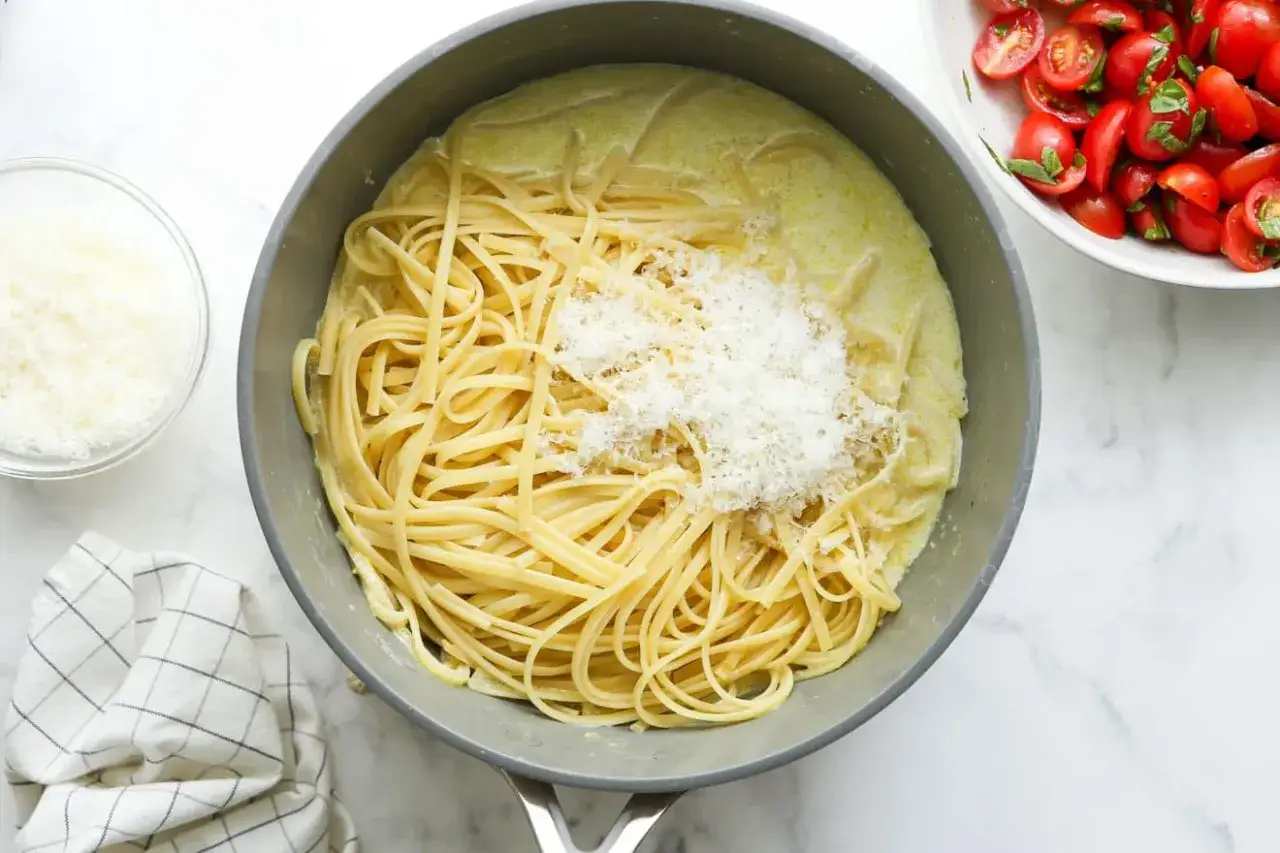 Enkel pasta med krämig sås och riven parmesan i en stekpanna. Bredvid syns en skål med körsbärstomater.