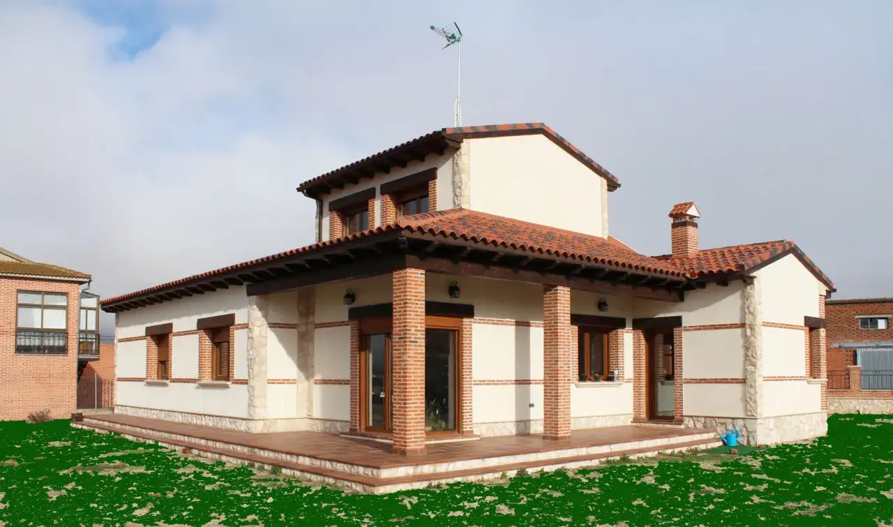 Casa con porche de obra, vigas de madera y tejado de tejas rojas. Césped verde y cielo nublado.